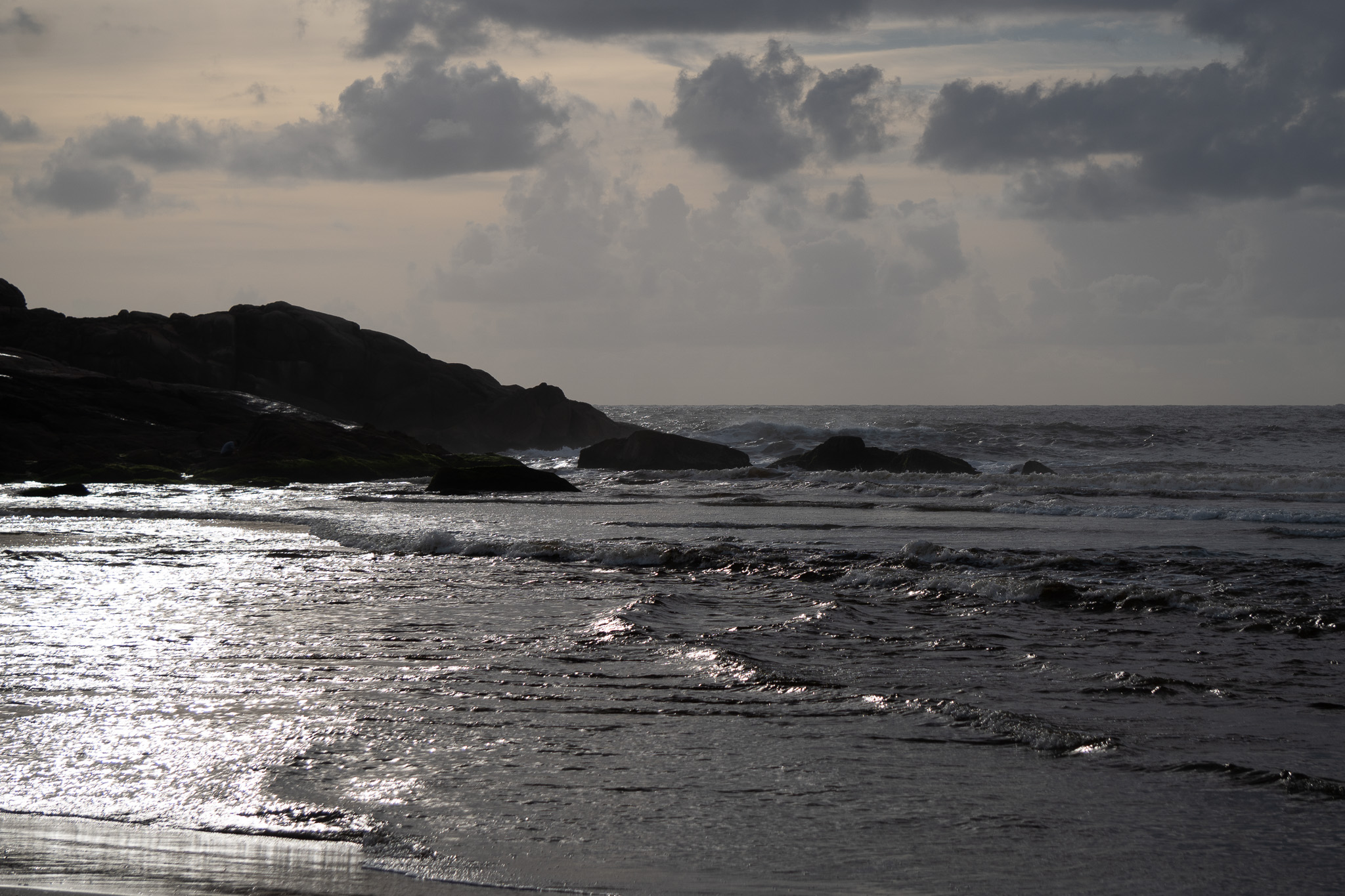 Rocky coastal headland silhouetted against sparkling ocean water under dramatic cloudy sky