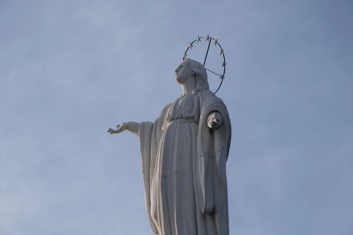 White statue of the Virgin Mary atop Cerro San Cristóbal with outstretched arm and star-crowned halo against clear blue sky