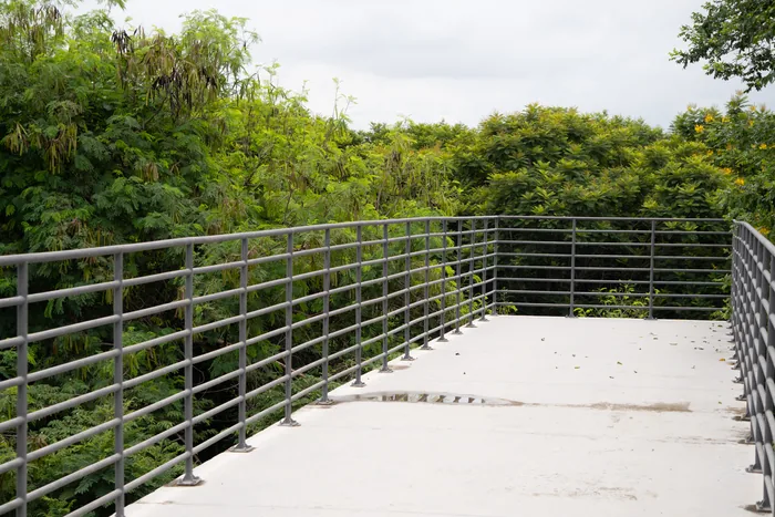 A raised concrete observation deck with metal railings overlooking a sea of green forest canopy under a cloudy sky.