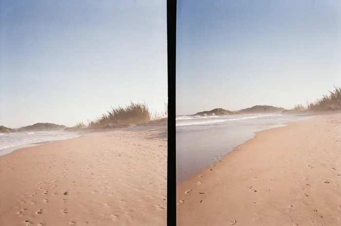 Film diptych showing two views of Ferrugem Beach with footprints in the sand, coastal vegetation, and a hill in the background under a pale blue sky.