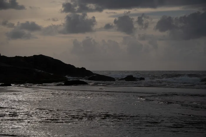 Rocky coastal headland silhouetted against sparkling ocean water under dramatic cloudy sky