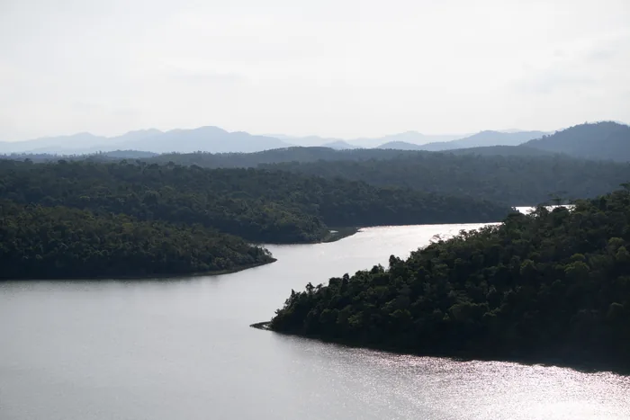 Aerial view of a lake winding through dense Atlantic Forest at Rio Doce State Park, with misty mountains in the background.