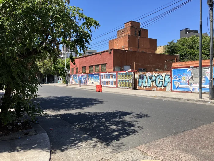 A red brick industrial building on a Buenos Aires street corner with graffiti murals on the surrounding walls, under a bright blue sky.